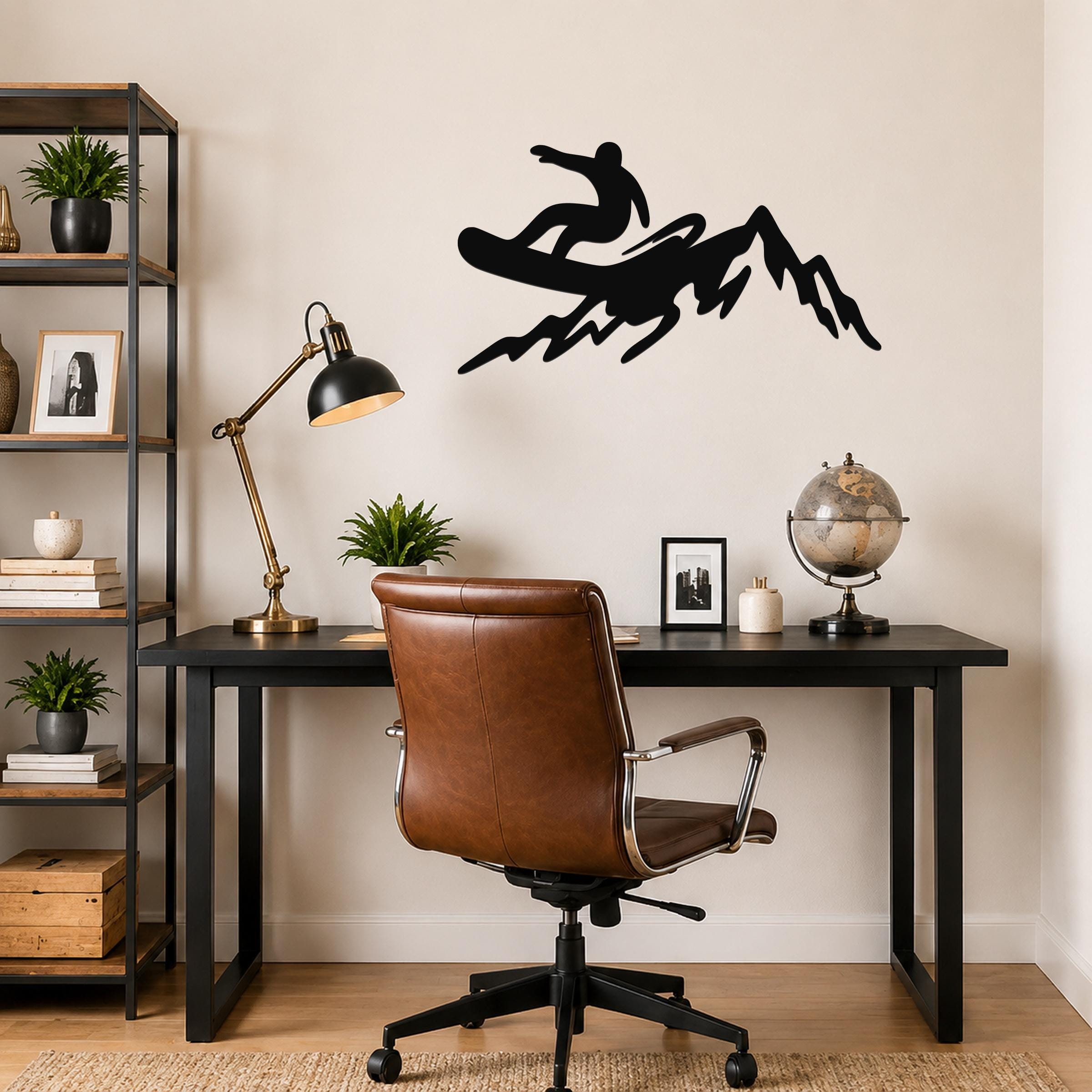 Black metal wall art silhouette of a snowboarder on a mountain, mounted above a black desk in a home office.