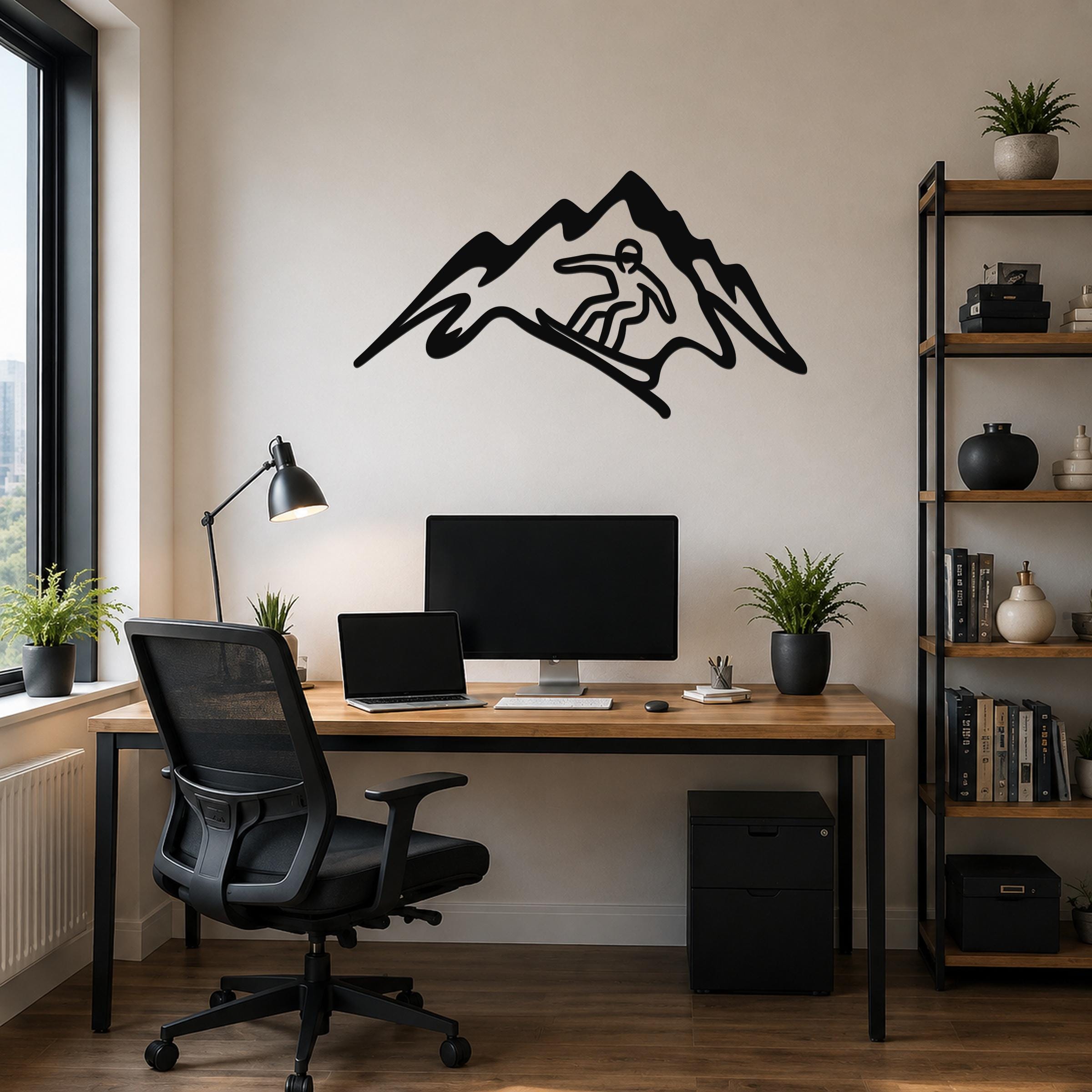 Black metal wall art with a snowboarder silhouette cutout inside a mountain shape, mounted above a wooden desk in a home office.
