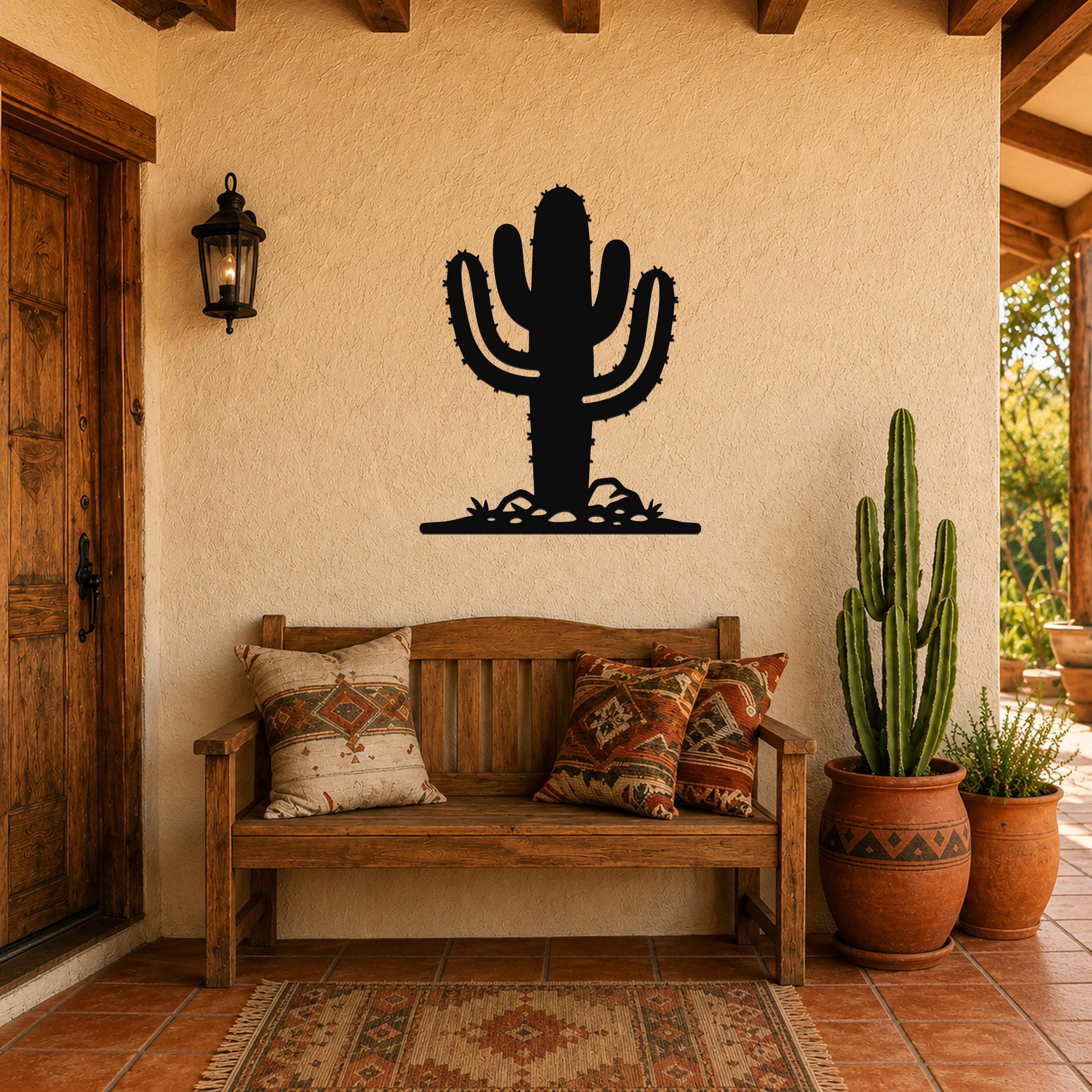 Black metal saguaro cactus wall art with spines and base cutouts, mounted on a stucco wall above a wooden bench in a southwestern entryway.
