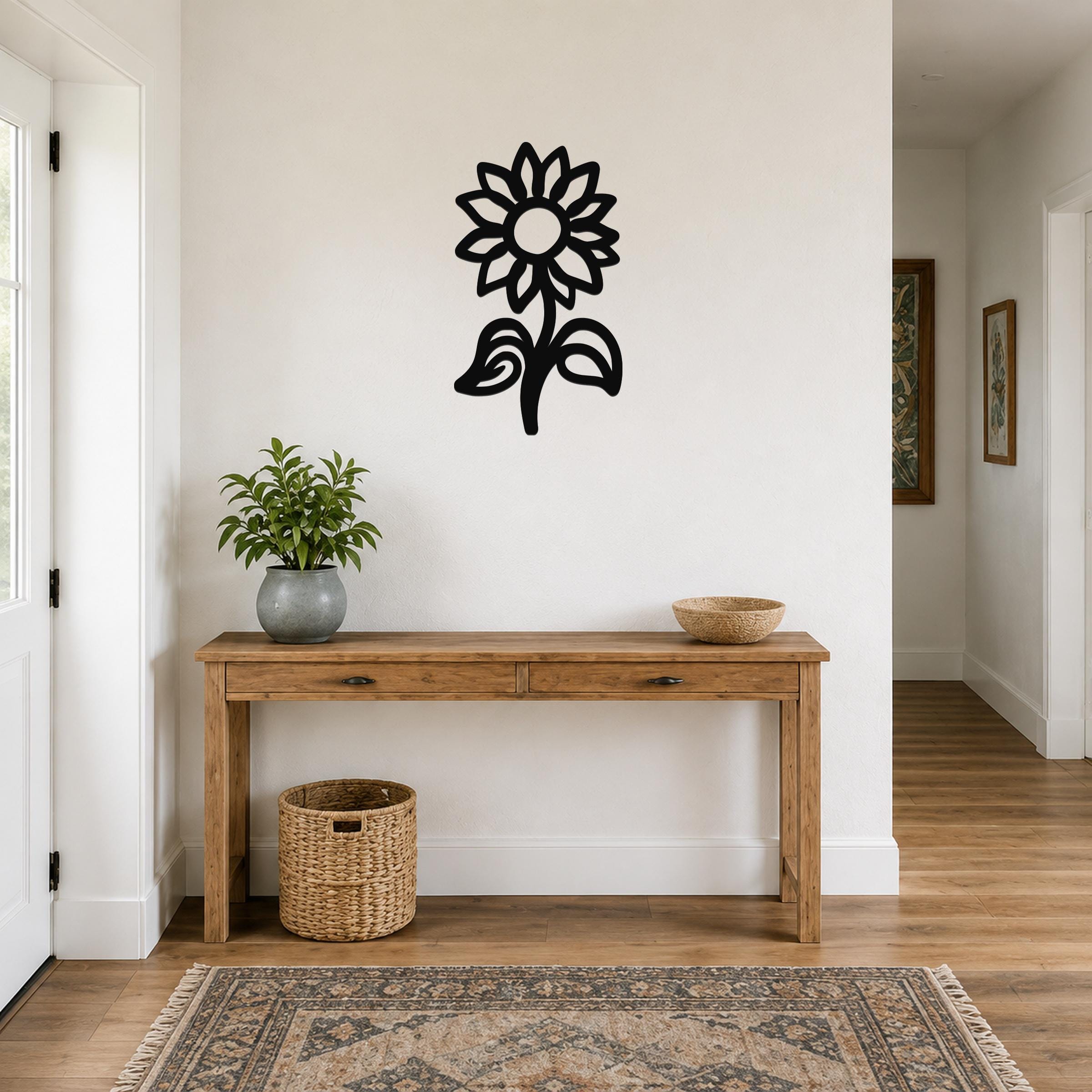 Black metal sunflower wall art with a silhouette design, mounted on a white wall above a wooden console table in a hallway.