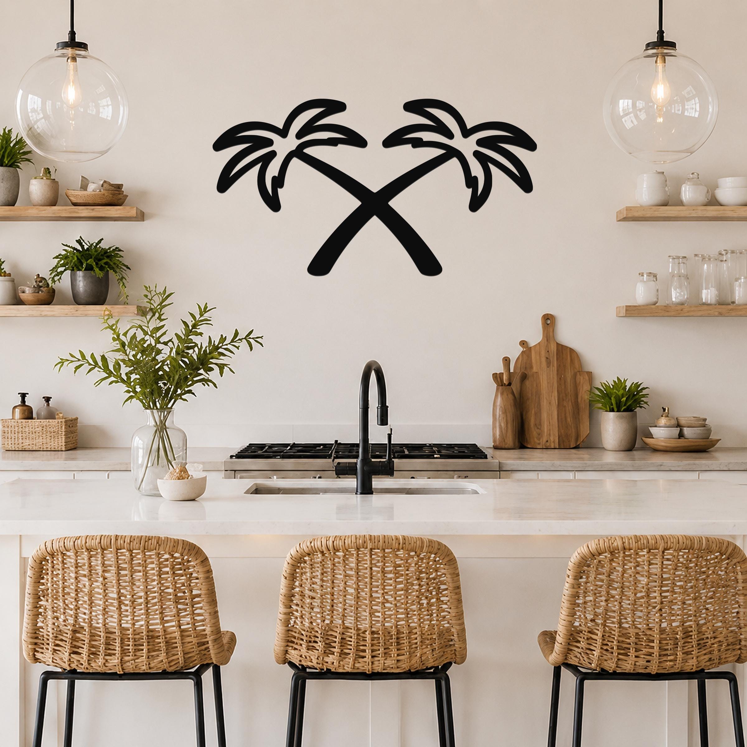 Black metal wall art featuring two crossed palm trees in silhouette, mounted on a kitchen wall above a counter with wicker bar stools.