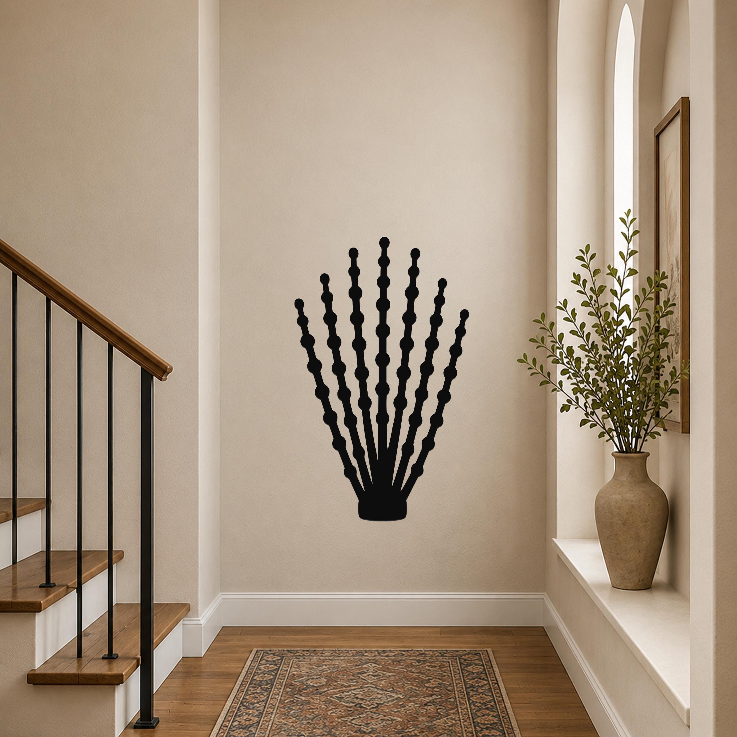Black metal wall art in the silhouette of an ocotillo plant with segmented stems, mounted on a hallway wall above a patterned rug.