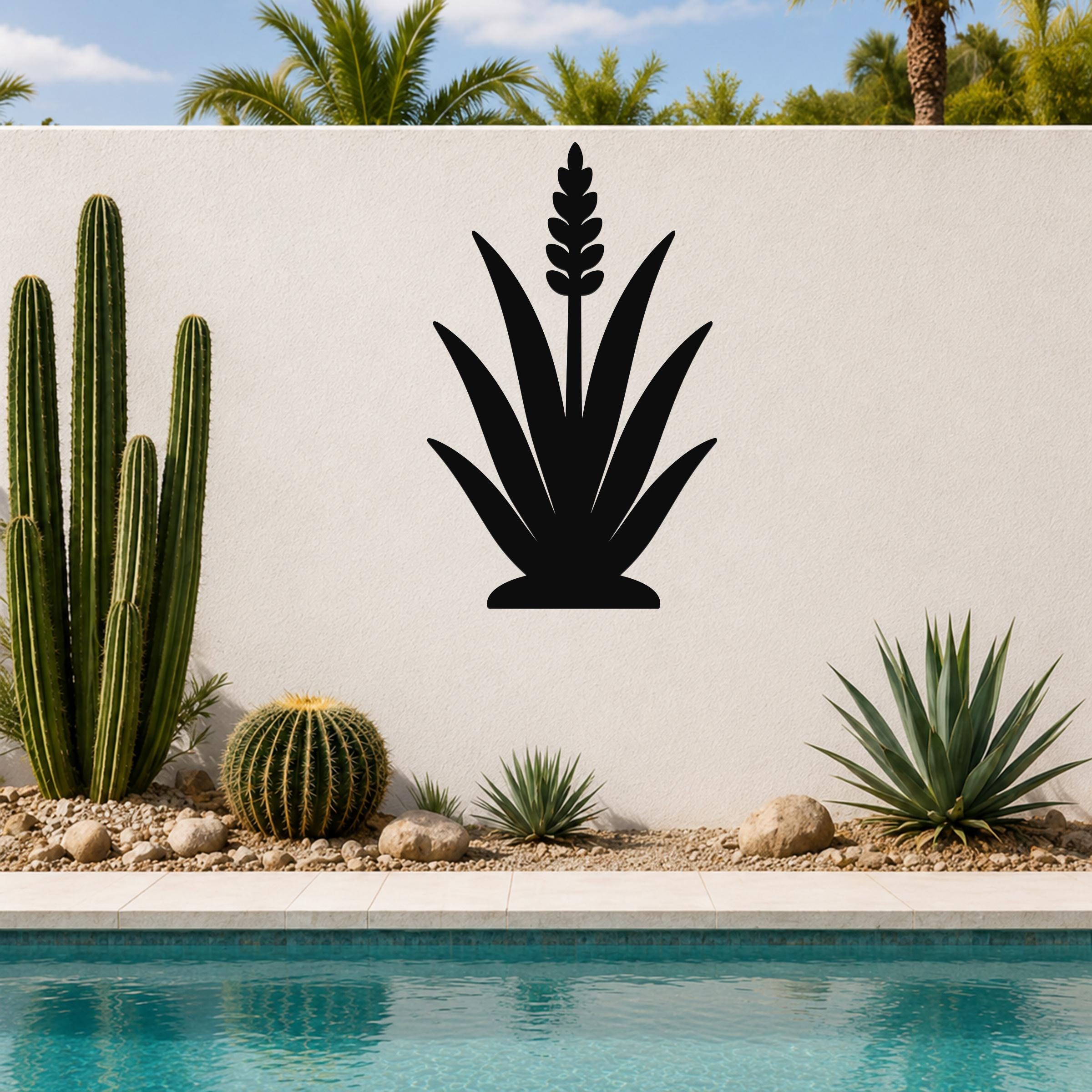 Black metal agave wall art with a tall flower spike cutout, mounted on a white outdoor wall above a poolside garden.