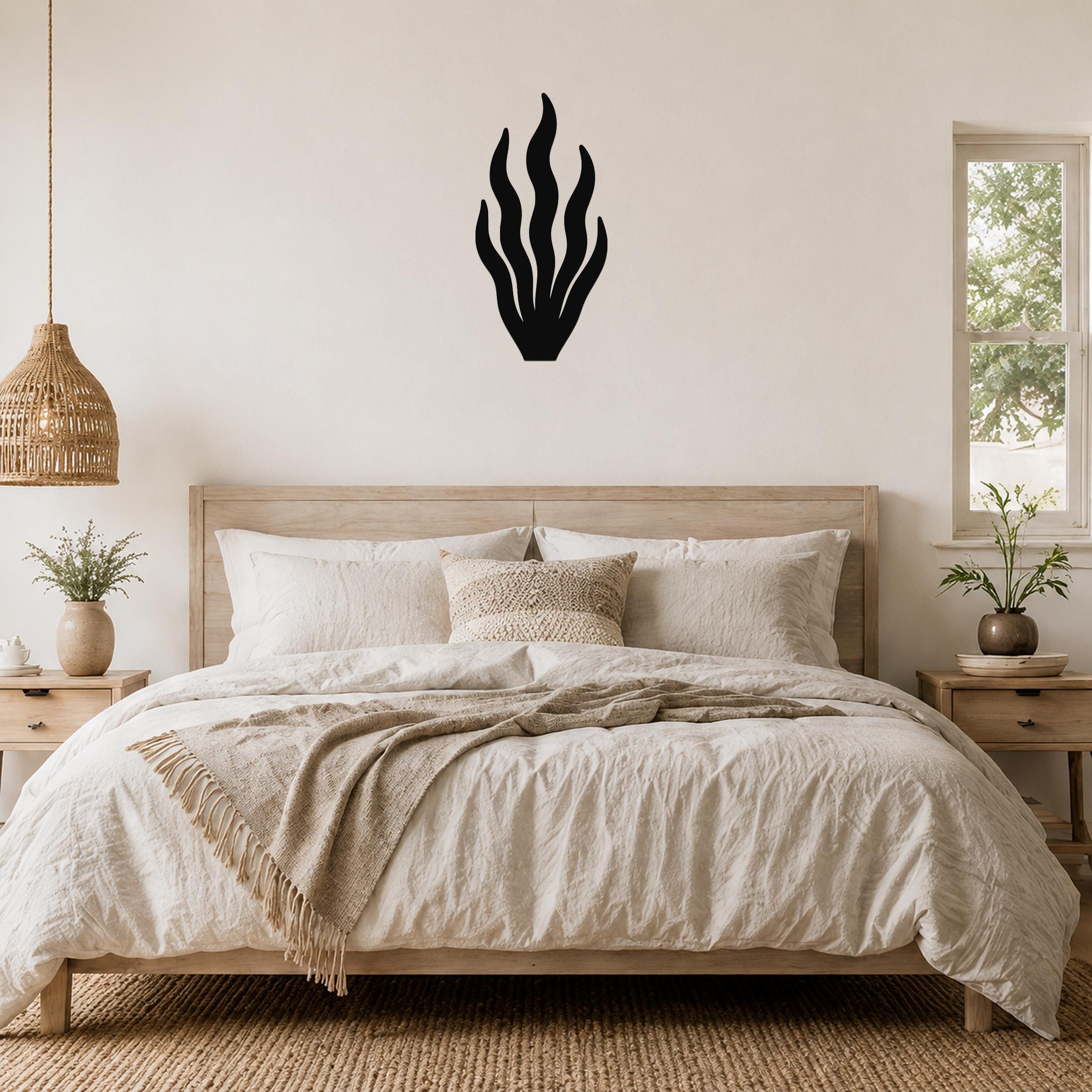 Black metal kelp wall art with flowing leaf cutouts, mounted above a wooden bed in a neutral bedroom.