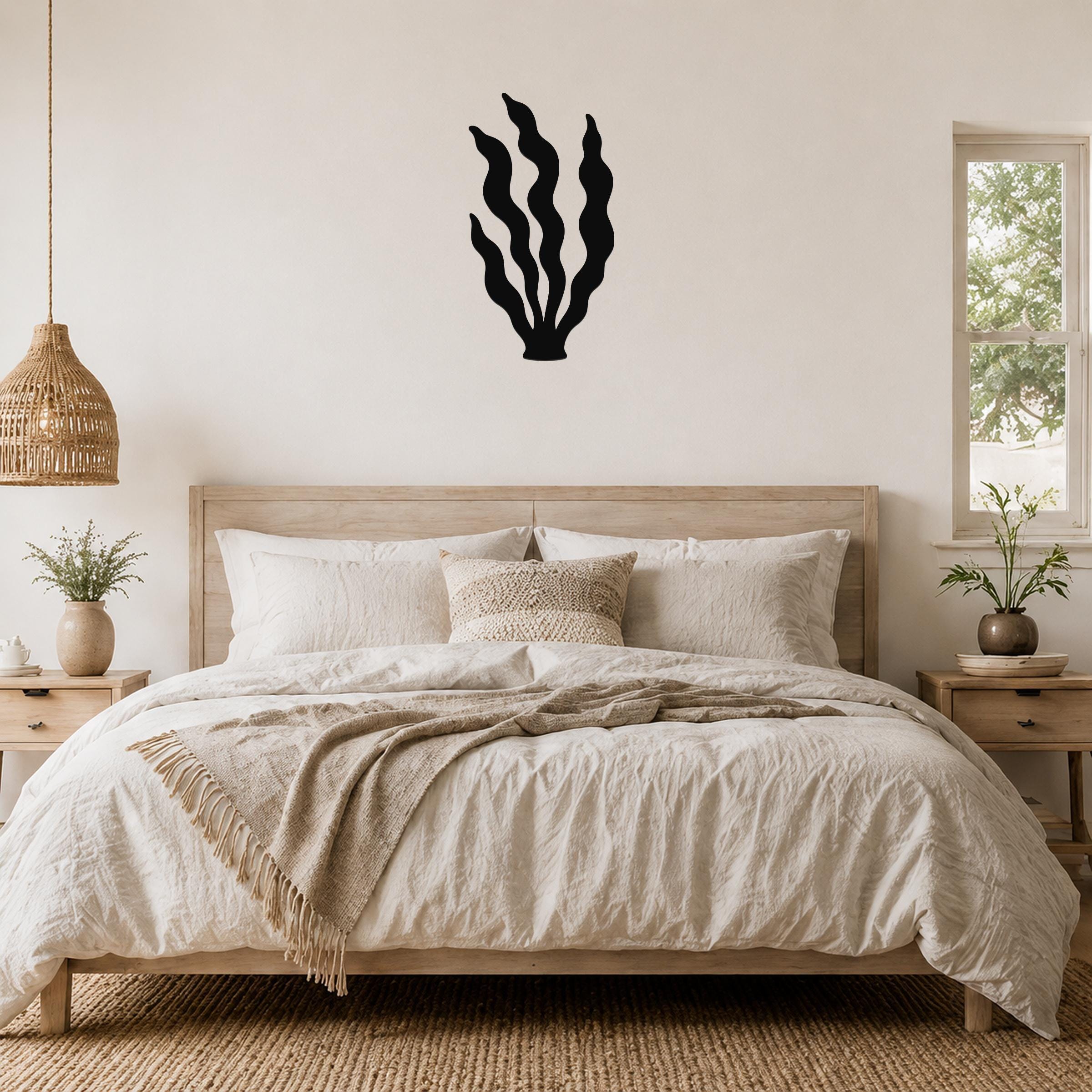 Black metal kelp wall art with wavy frond cutouts, mounted above a wooden bed in a neutral bedroom.