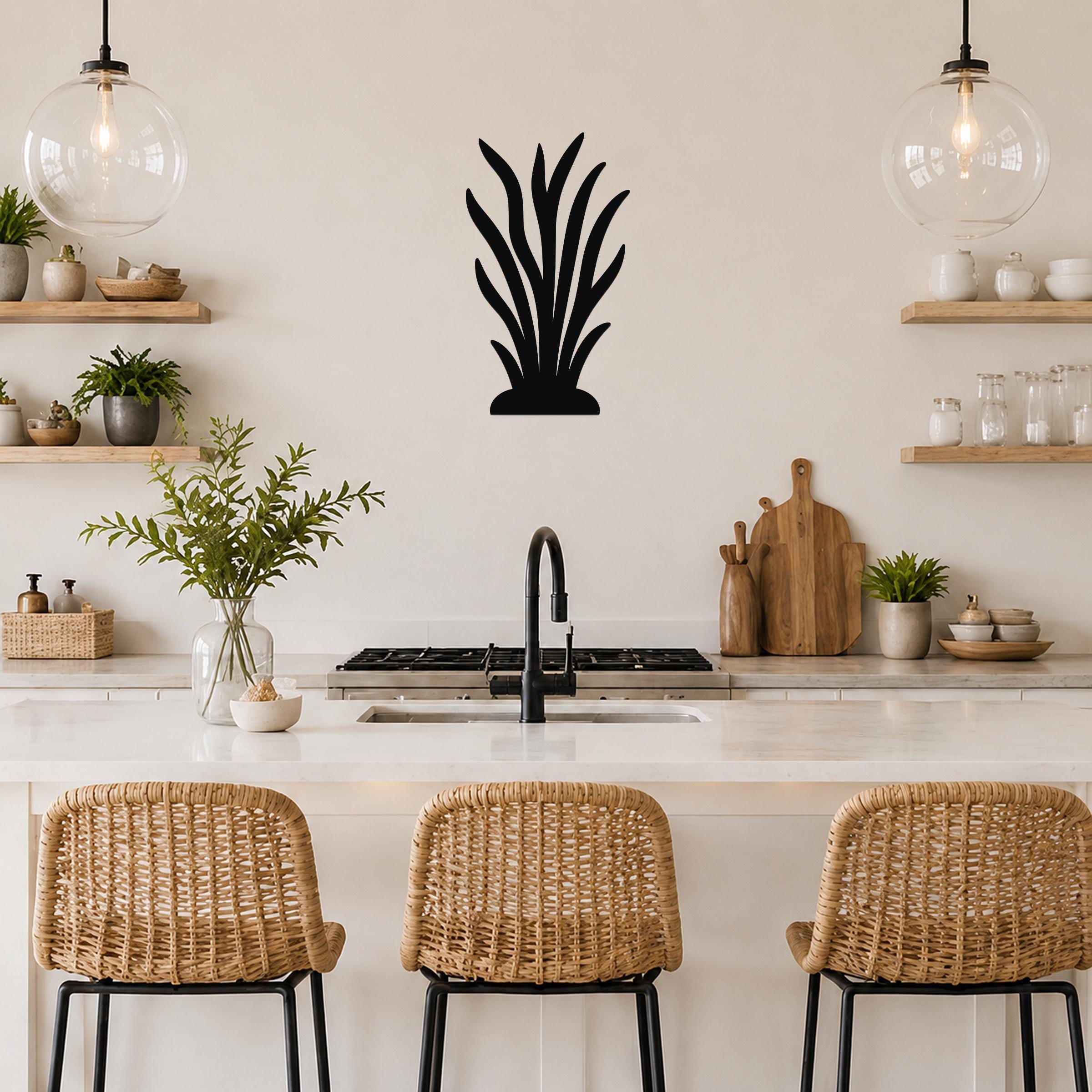 Black metal kelp wall art silhouette mounted on a kitchen wall above a counter, with wicker bar stools and pendant lights visible below.