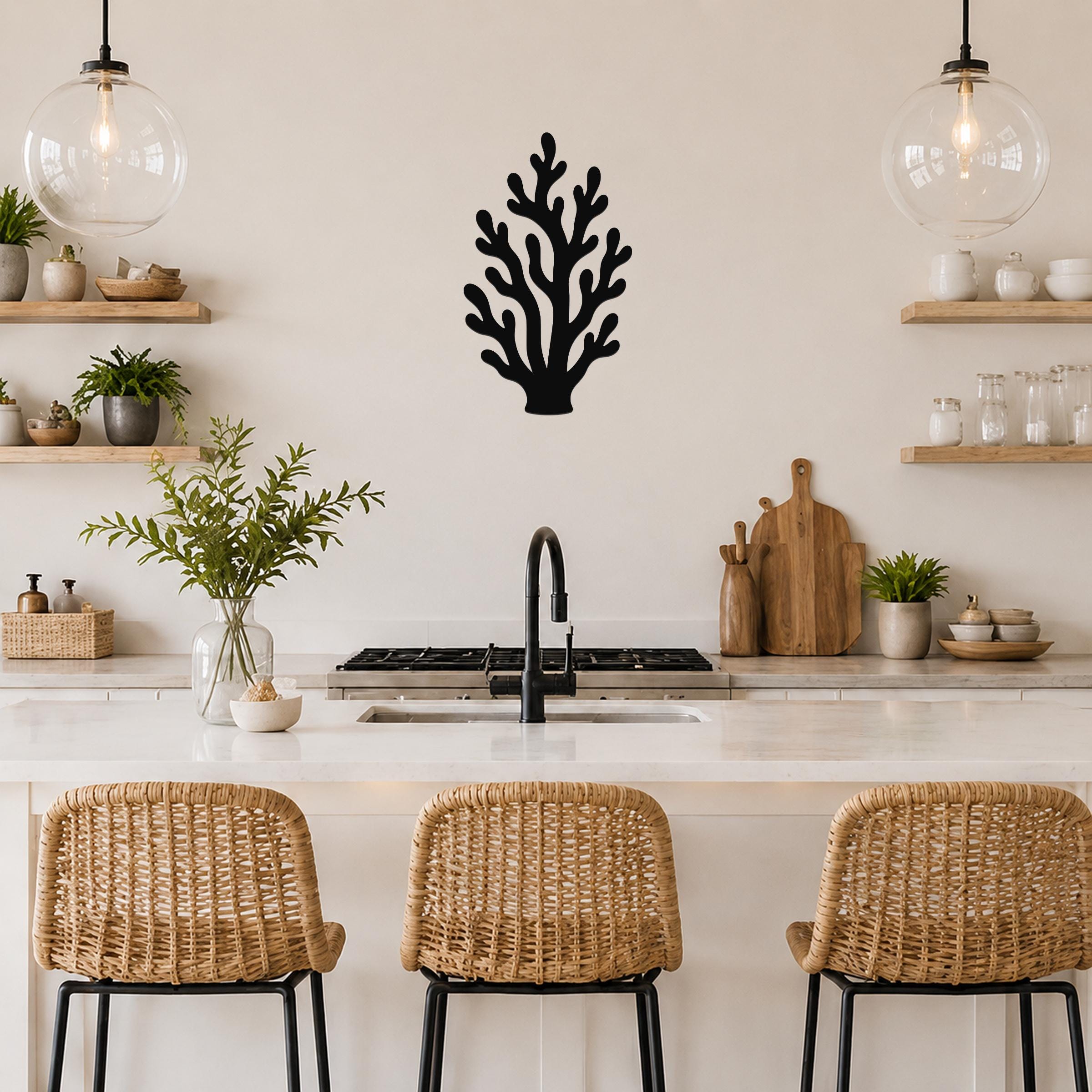 Black metal coral wall art with branching cutouts, mounted on a kitchen wall above a counter between two glass pendant lights.