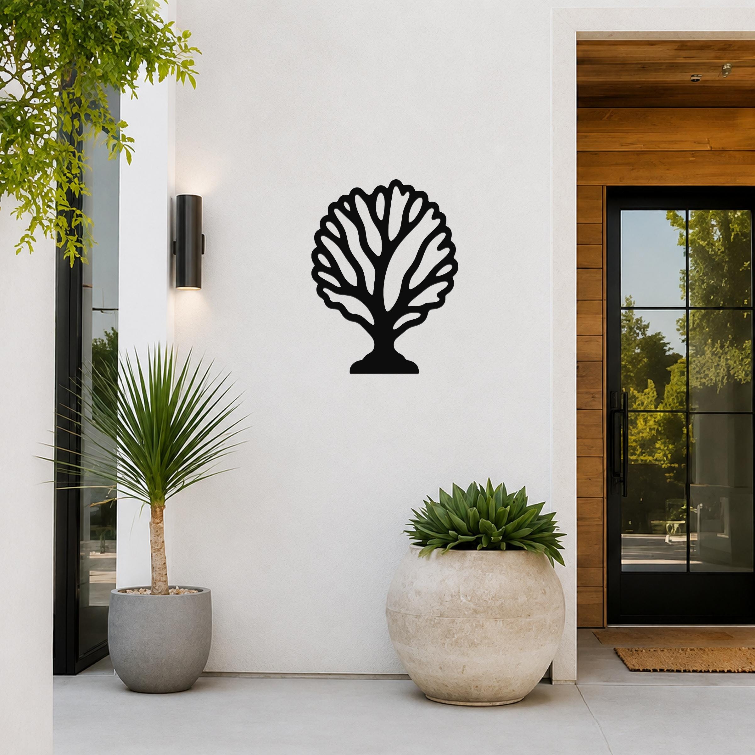 Black metal fan coral wall art with intricate branching cutouts, mounted on a white exterior wall beside a glass door and potted plants.