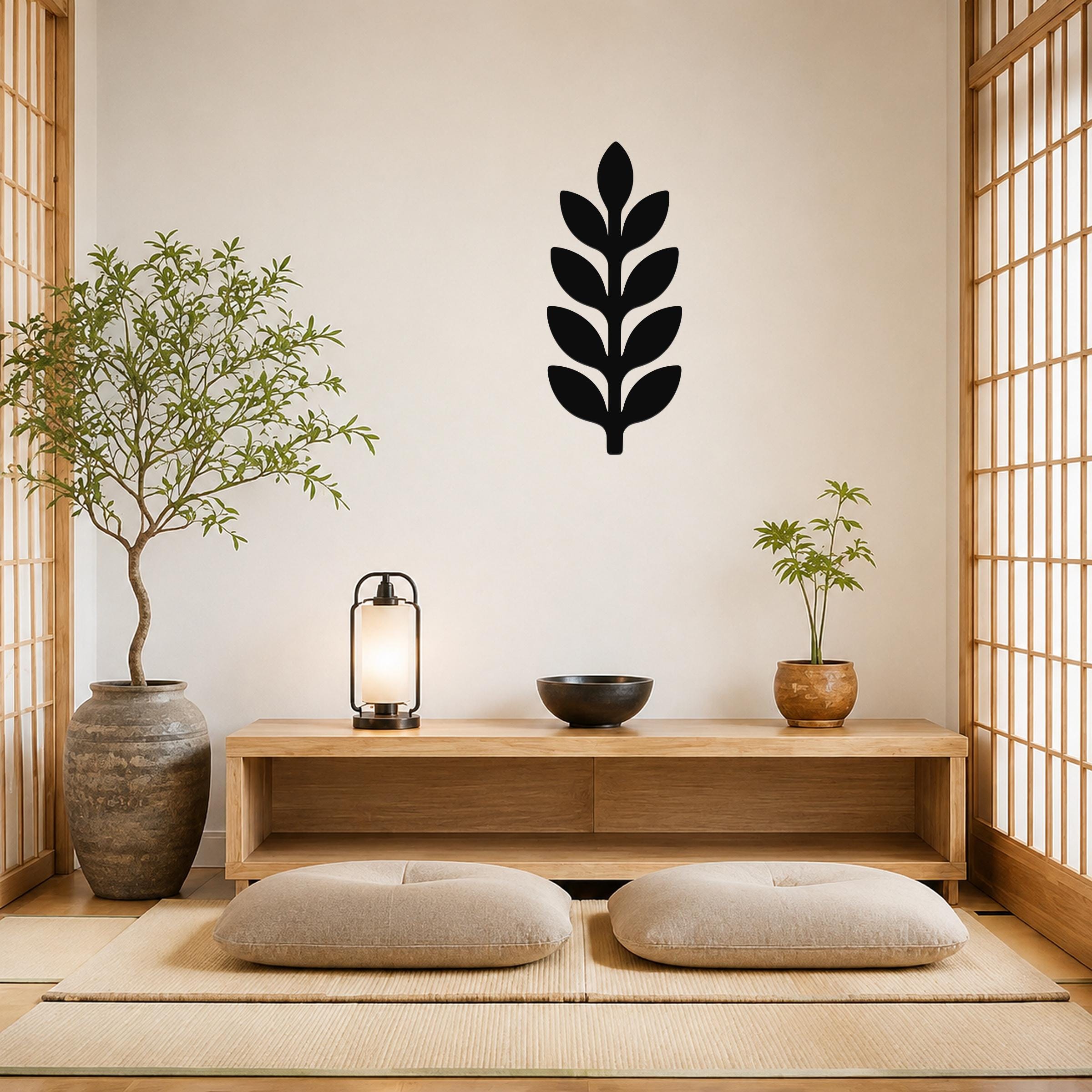 Black metal wall art in a leafy sprig silhouette, mounted on a light-colored wall above a wooden console in a minimalist living room.