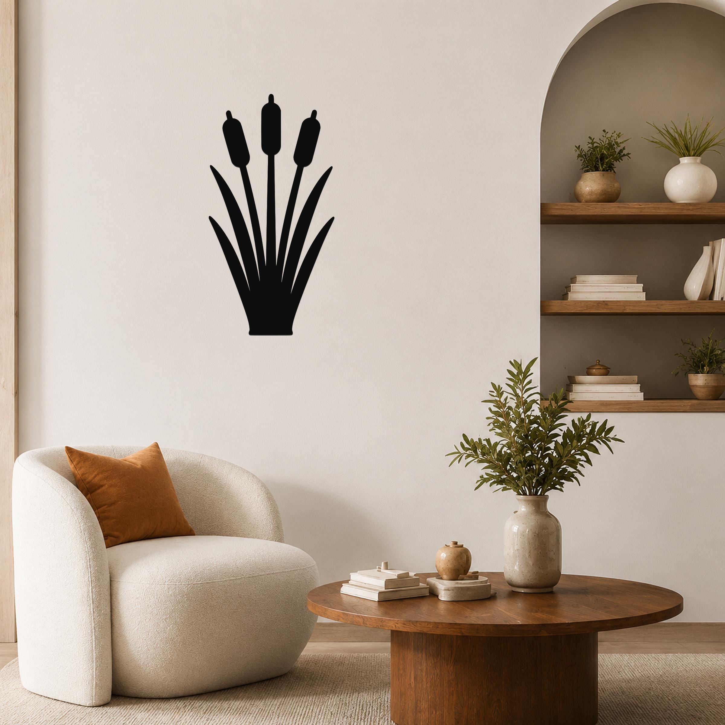 Black metal cattail wall art silhouette mounted on a living room wall above a white armchair.