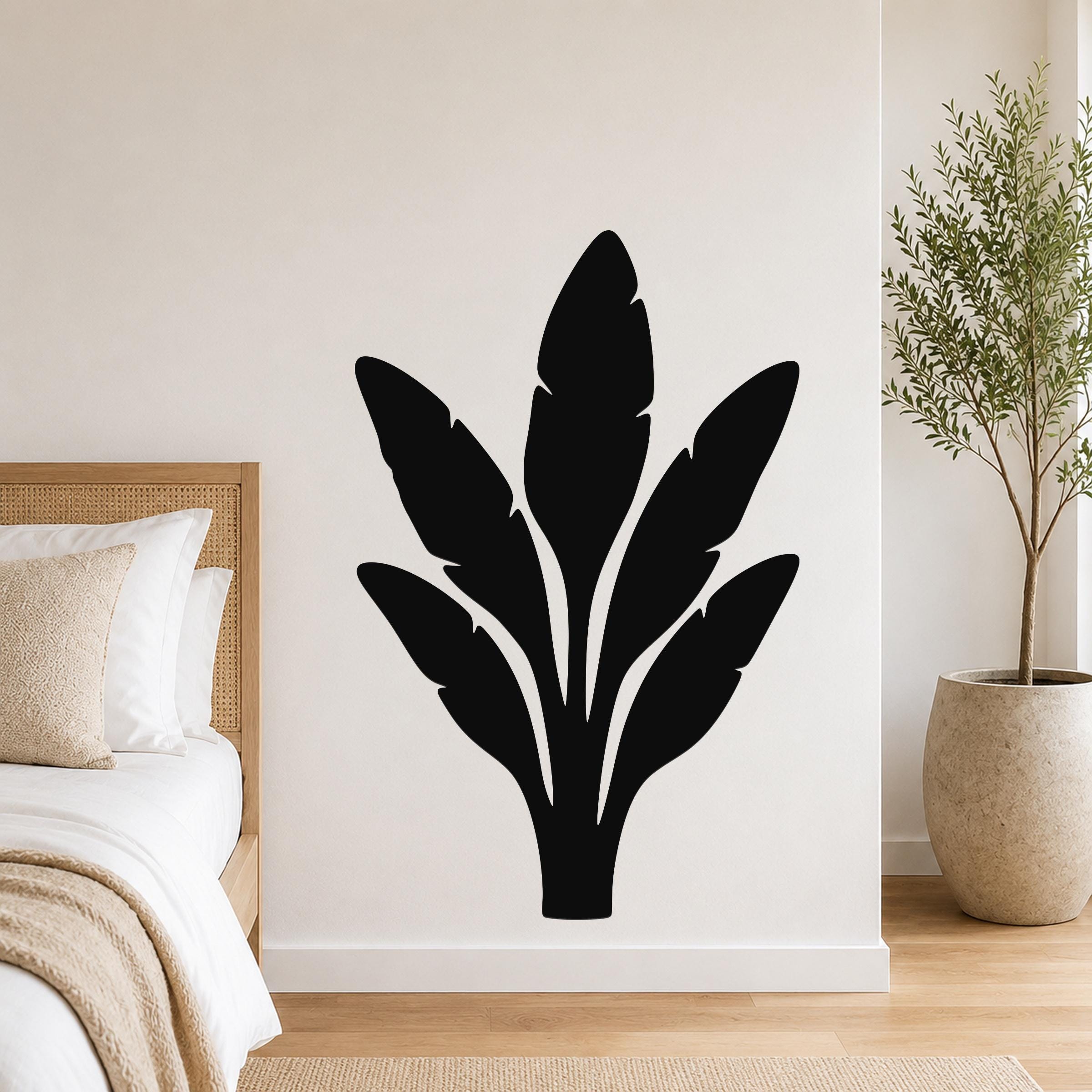 Black metal wall art in a bold banana plant silhouette with layered leaf cutouts, mounted on a bedroom wall above a bed.
