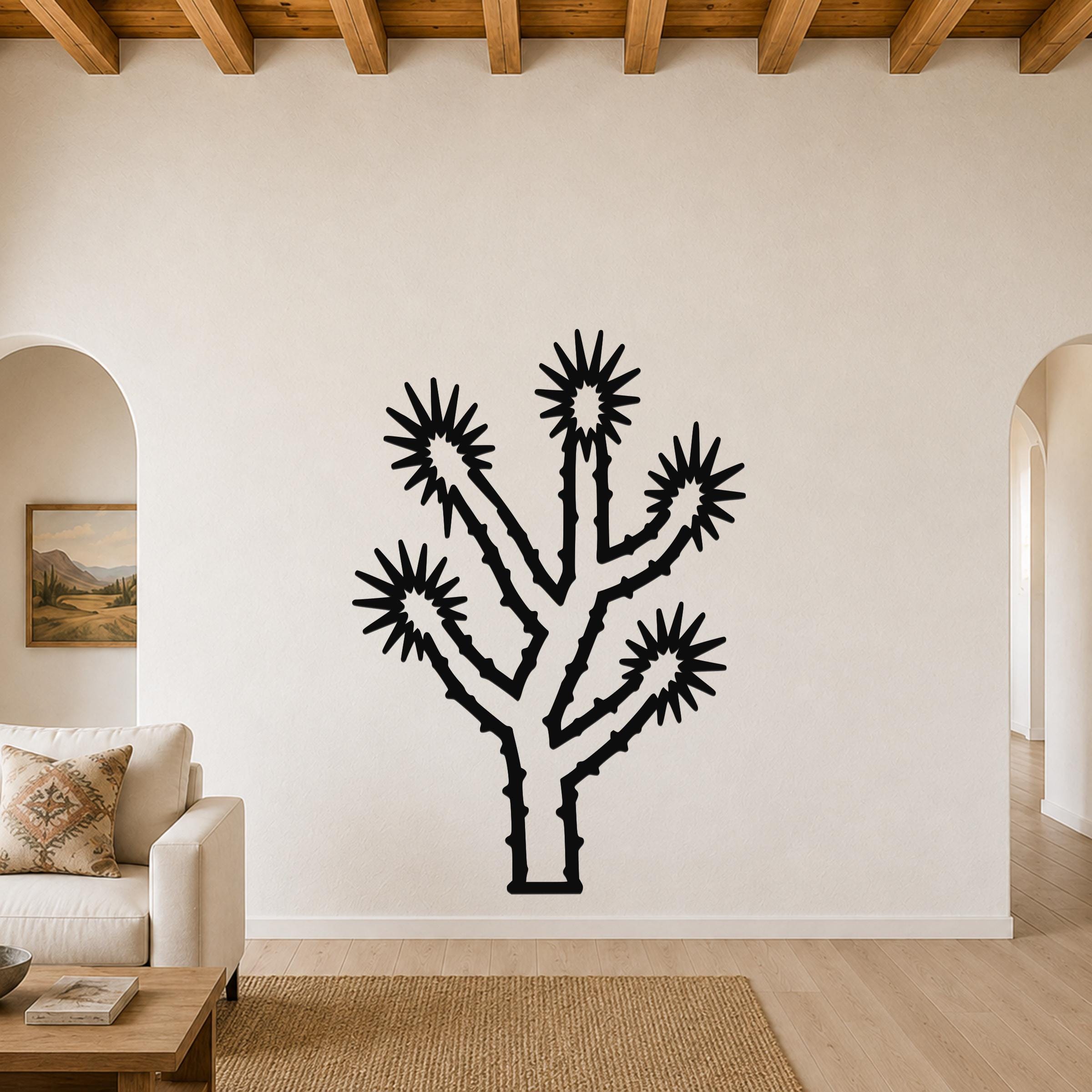 Black metal Joshua tree wall art with spiky branch cutouts, mounted on a living room wall above a sofa.