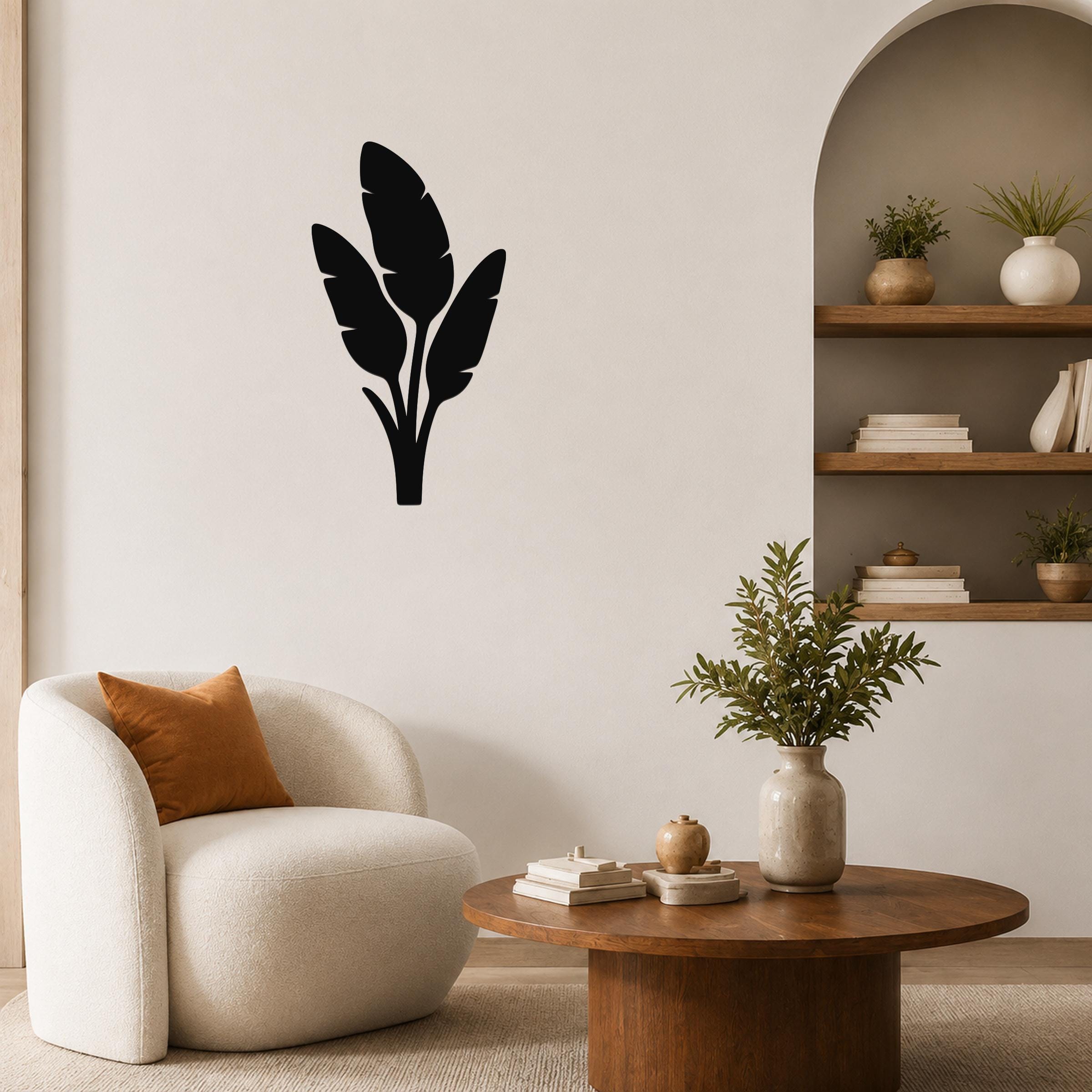 Black metal wall art featuring a tropical leaf silhouette, mounted on a living room wall above a round wooden coffee table.