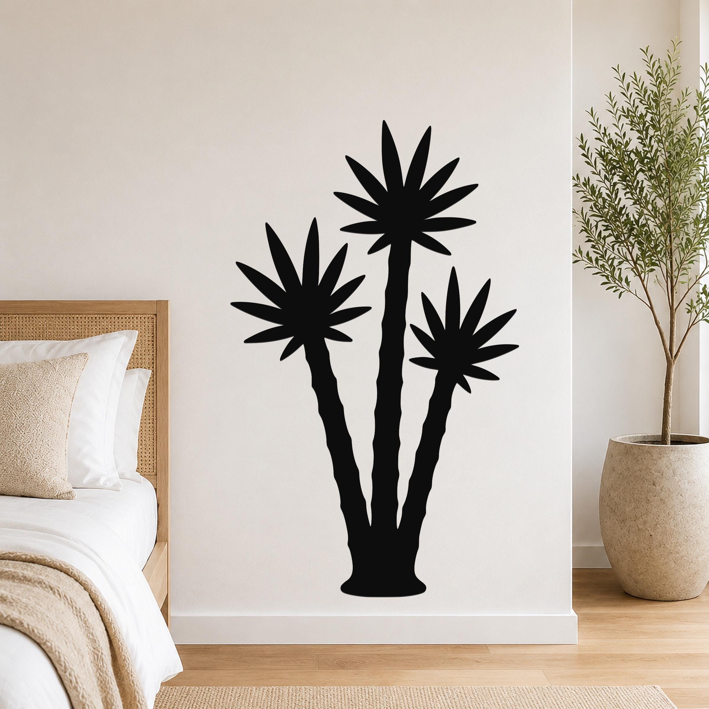 Black metal wall art featuring a silhouette of three abstract palm trees, mounted on a bedroom wall above a bed.