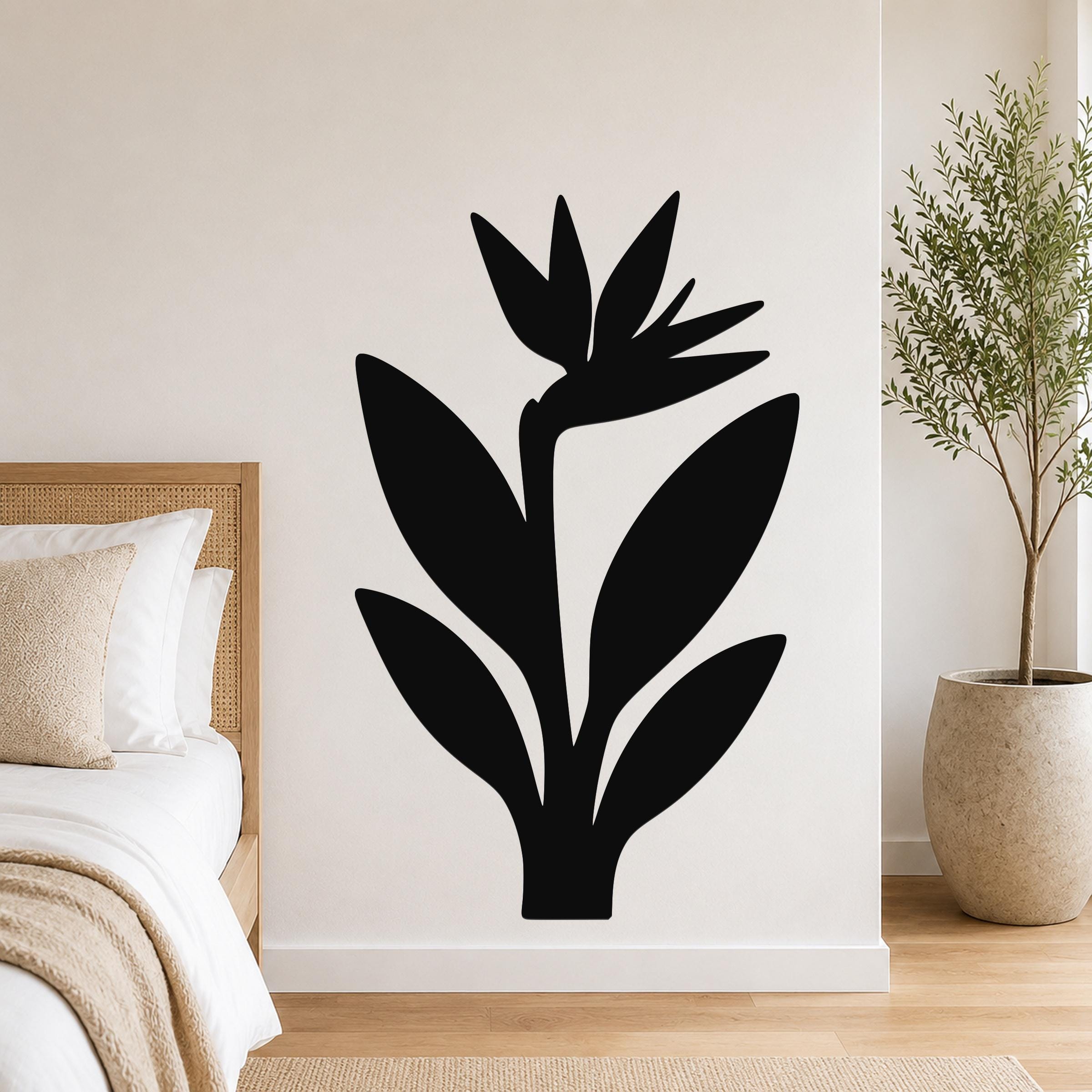 Black metal wall art in a Bird of Paradise silhouette, mounted on a white bedroom wall above a bed with a woven headboard.