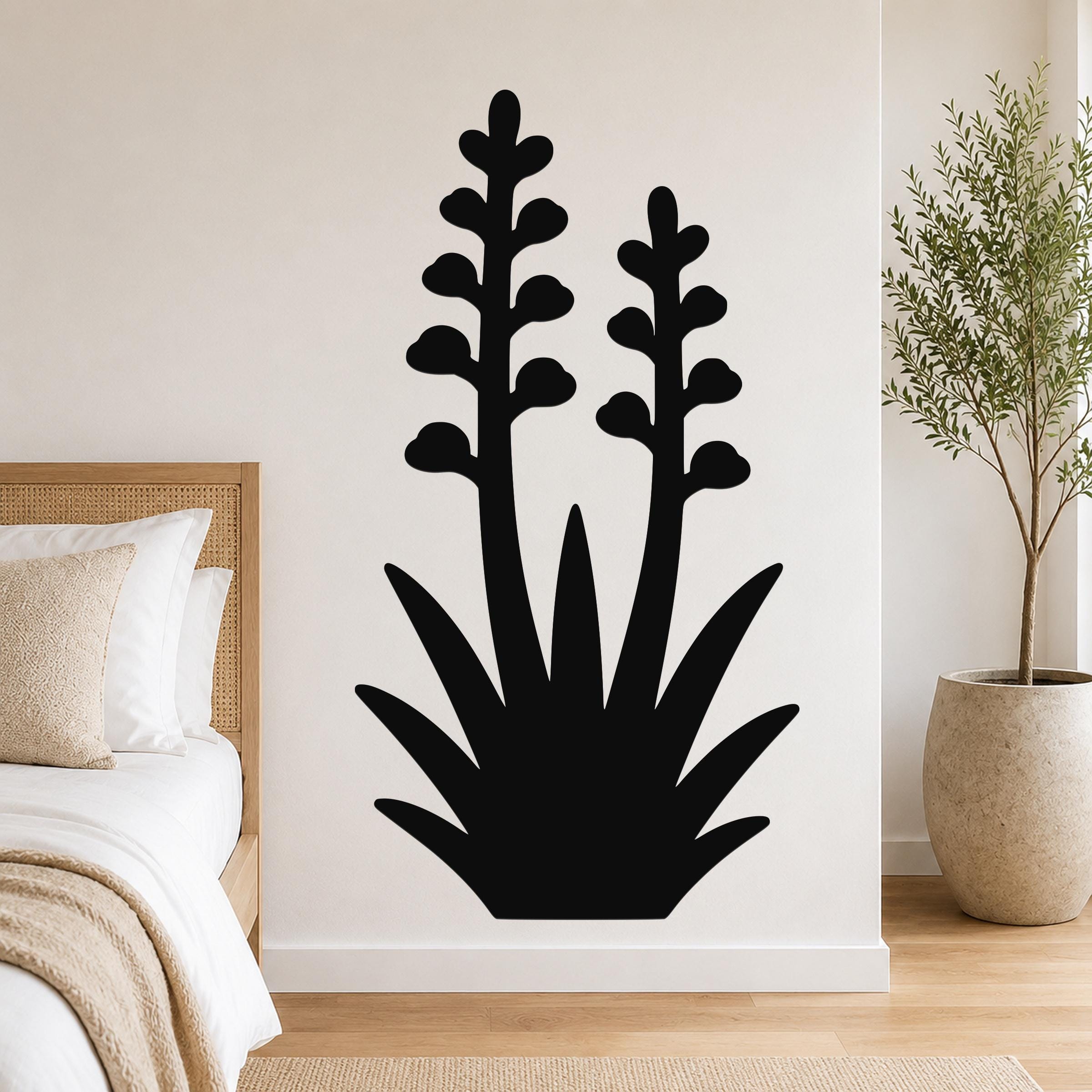 Black metal wall art in a silhouetted agave plant shape with two tall flower stalks, mounted on a bedroom wall above a bed.