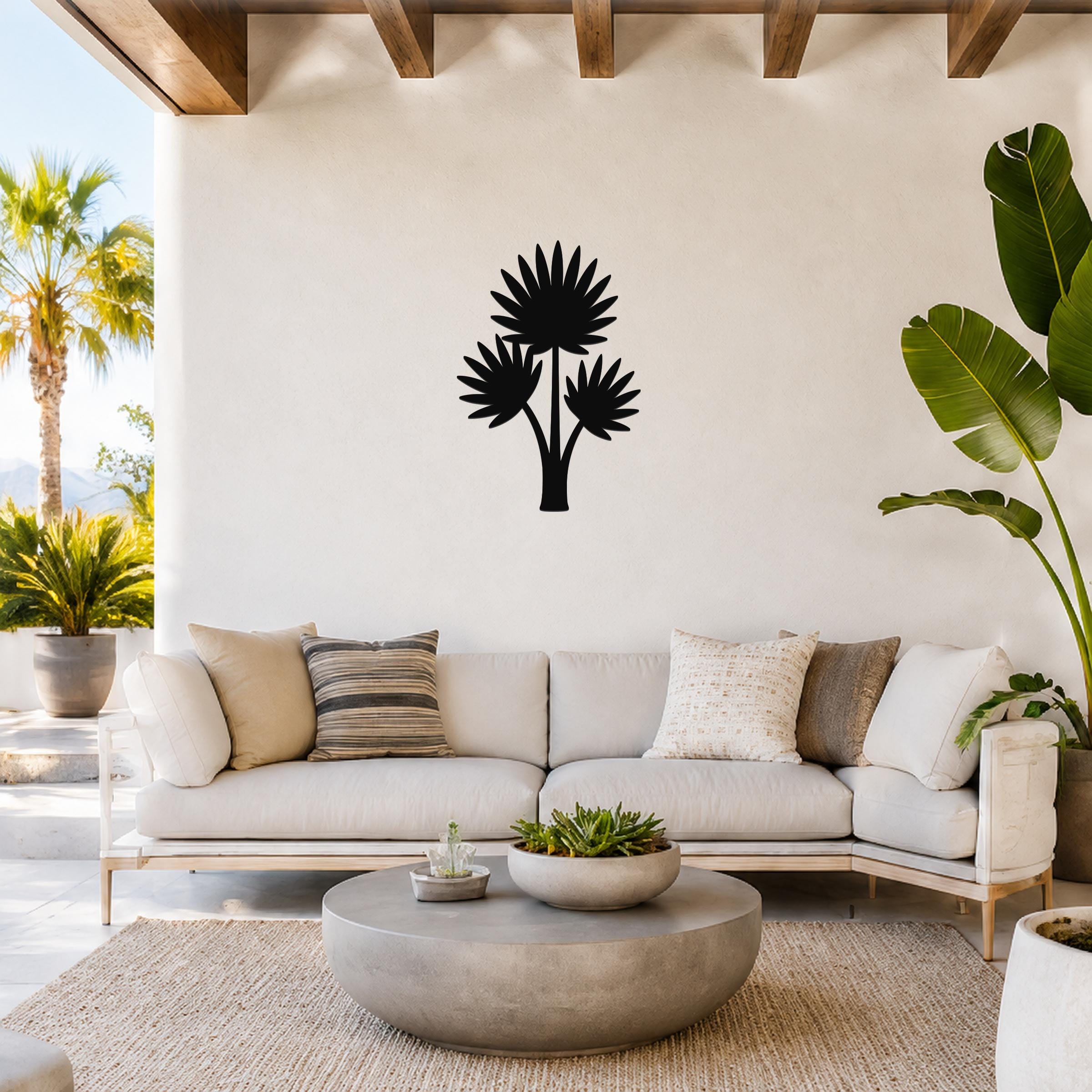 Black metal wall art featuring a fan palm tree silhouette with three fronds, mounted on a white wall above a light-colored sofa in a bright living room.