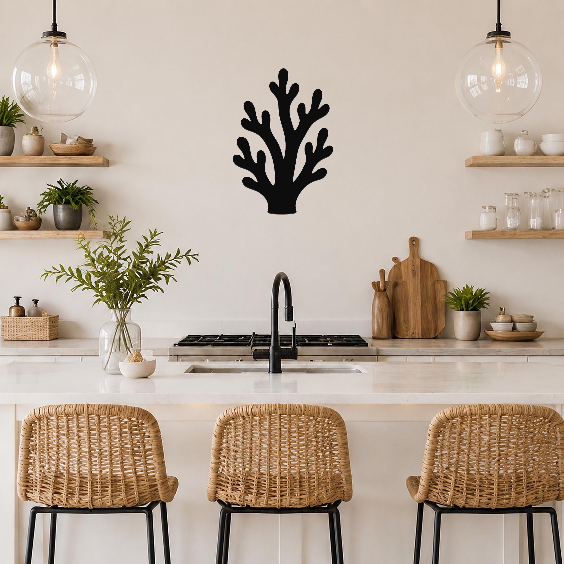 Black metal branching coral wall art with cutout details, mounted on a kitchen wall above a counter between two glass pendant lights.