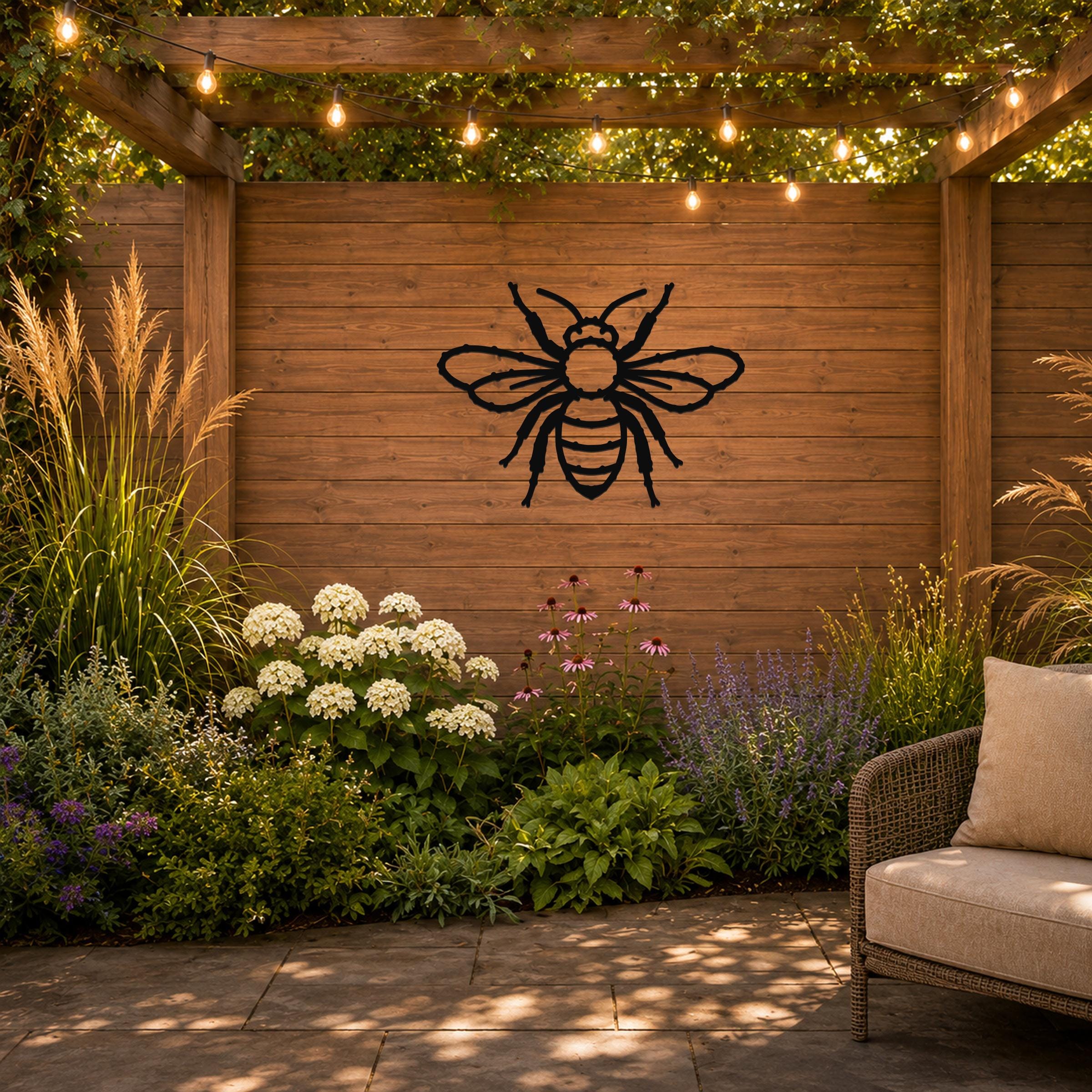 Black metal bee wall art with detailed cutout wings and body, mounted on a wooden fence in a garden patio setting.