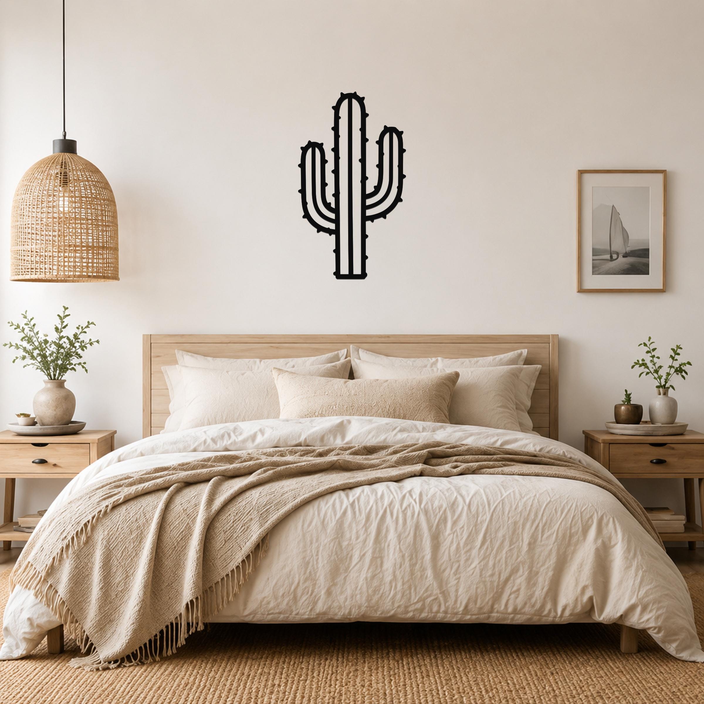 Black metal wall art in the silhouette of a saguaro cactus with spines, mounted on a wall above a bed in a neutral bedroom.