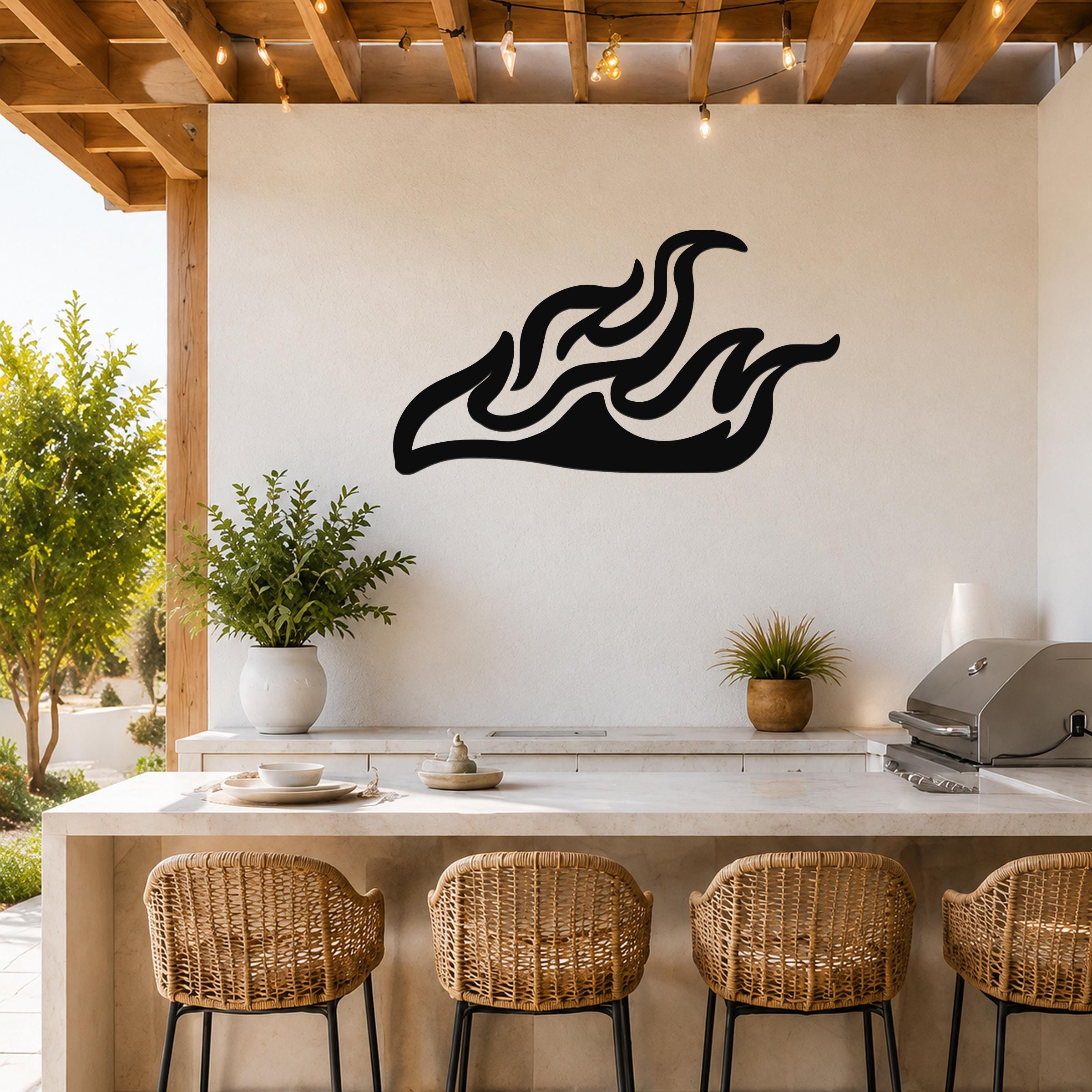Black metal flame wall art with flowing silhouette cutouts, mounted on a white outdoor kitchen wall above a counter.