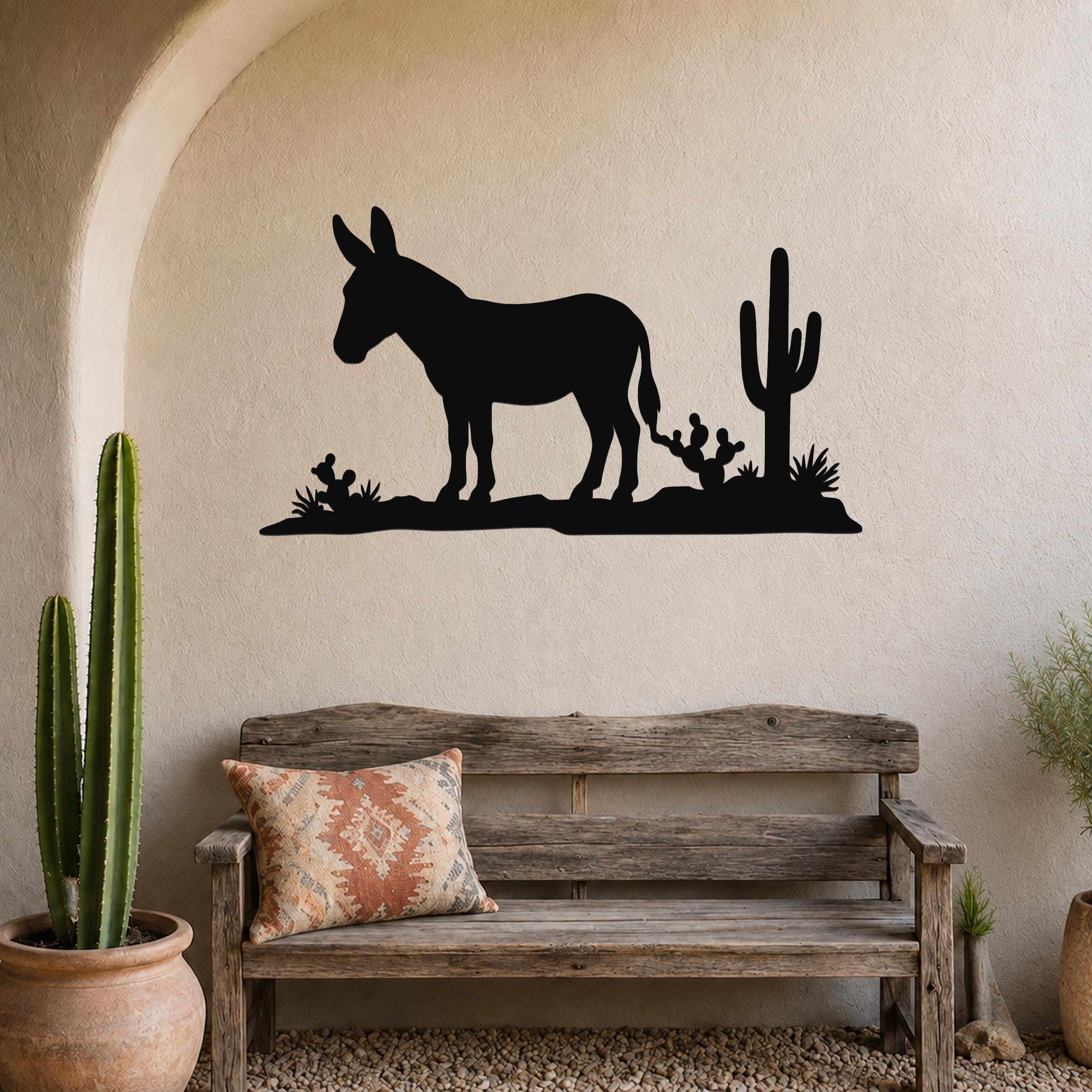 Black metal wall art silhouette of a burro and cacti, mounted above a wooden bench in a rustic indoor space.