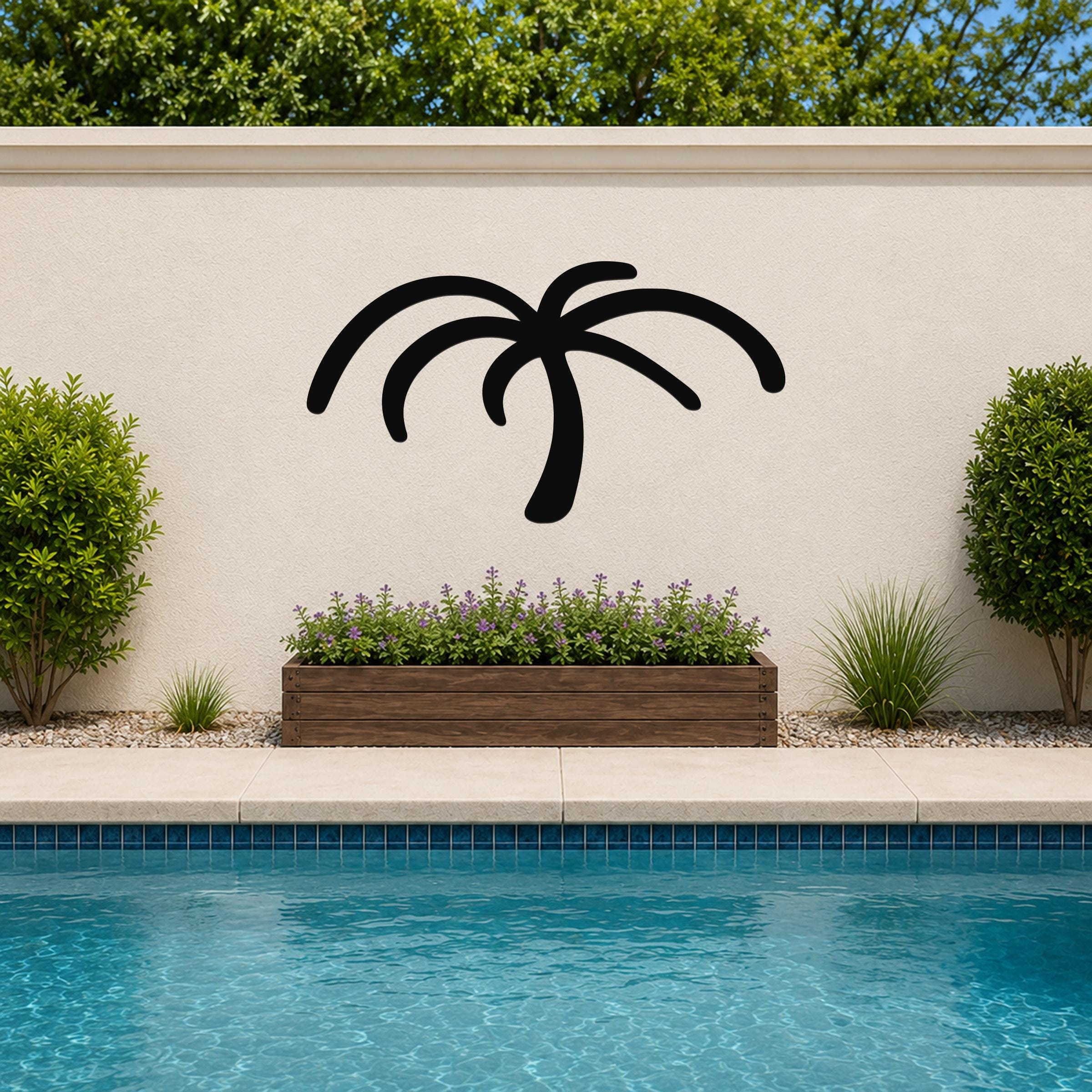 Black metal palm tree wall art silhouette mounted on a beige outdoor wall above a planter and pool.
